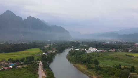 Aerial-Evening-View-Of-Vang-Vieng-With-Nam-Xong-River-Running-Through-Landscape