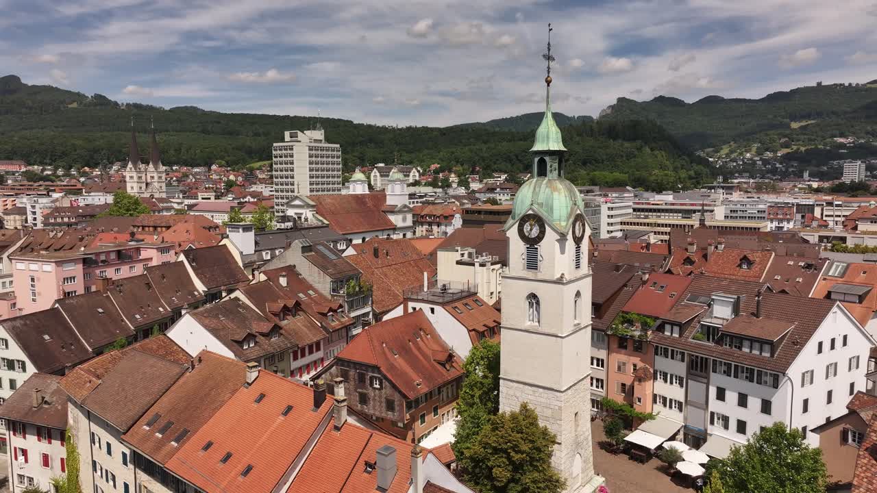 Luftaufnahme von Olten, Schweiz, die die roten Ziegeldächer der Stadt, historische Gebäude und den markanten Uhrturm mit seiner grünen Kupferkuppel zeigt. Die umliegenden Hügel umrahmen das Stadtgebiet