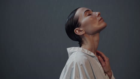 young woman with wet hair tied in a braid meditates with closed eyes, wearing a white shirt, against a dark gray background, conveying a sense of tranquility and mindfulness