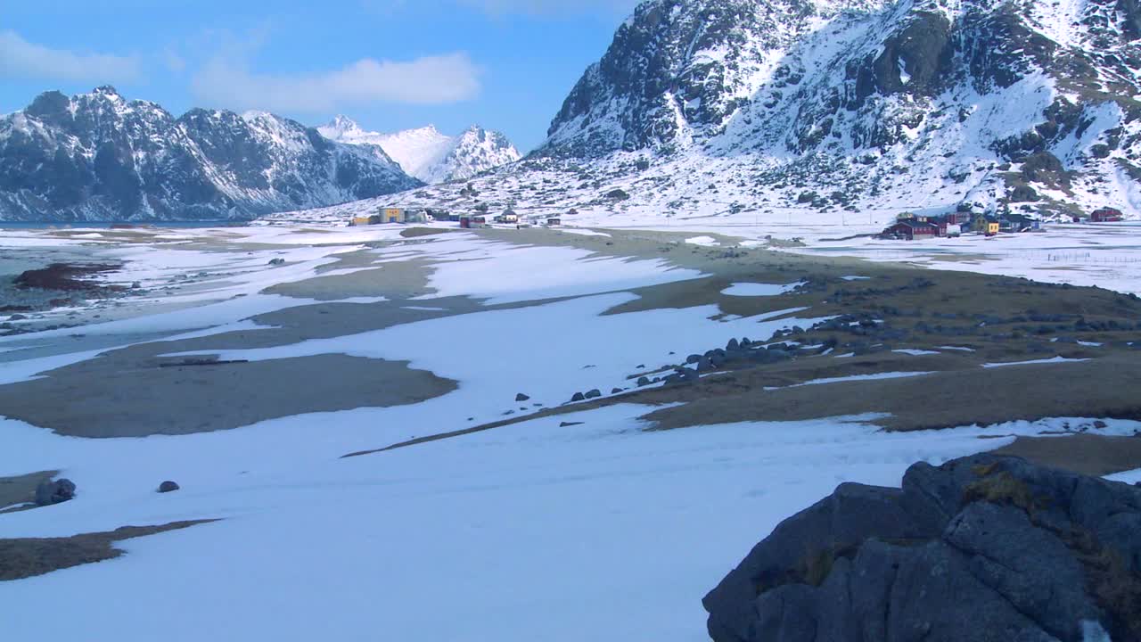 Bølger ruller inn mot en vakker snødekt strand blant fjorder nord for polarsirkelen på Lofotøyene i Norge.