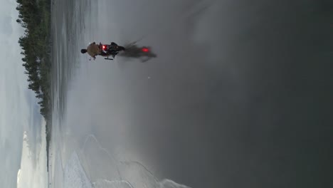 vertical aerial follows young man riding motorcycle on sandy beach