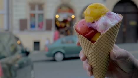 Vista-Cercana-En-Cámara-Lenta-De-Una-Mujer-Que-Comienza-A-Comer-Bolas-De-Helado-Contra-El-Paisaje-Urbano-Desenfocado-En-El-Fondo-De-Praga,-República-Checa