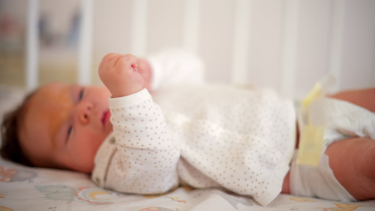 Un neonato in vestiti morbidi si muove delicatamente in una culla, allungando le piccole mani nella luce naturale del mattino