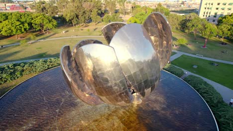 tilt down aerial view of the stainless steel petals of the floralis generica being illuminated by the sun's rays, round pool