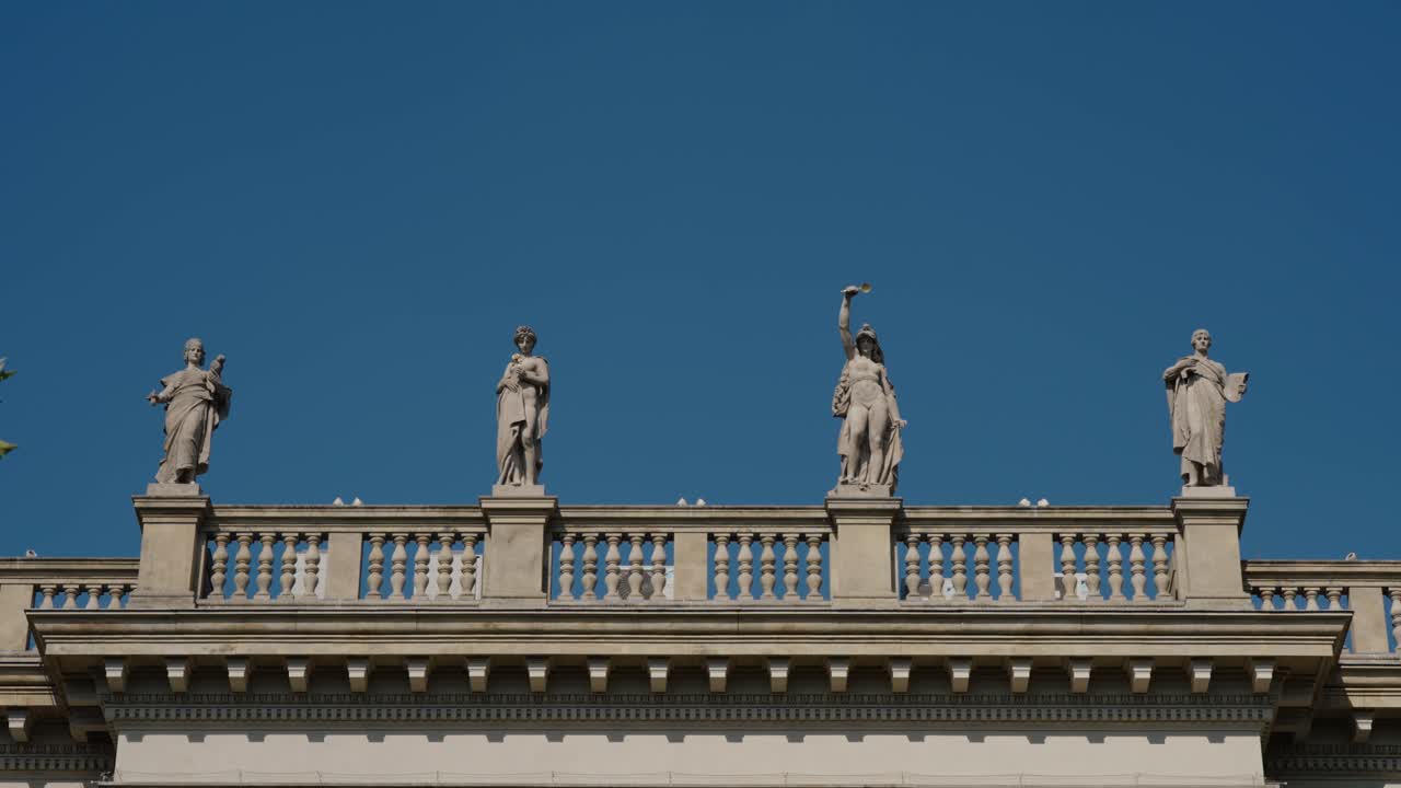 Four stone statues stand atop the balustrade of Prague’s National Museum under blue sky