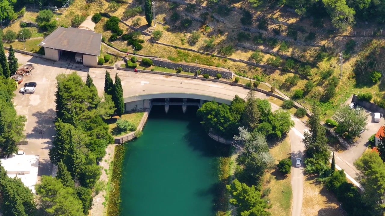 Ein Wasserkraftwerk nutzt den Flusslauf für saubere Energie. Eine Luftaufnahme zeigt Infrastruktur und Landschaft in ländlicher Gegend. Die Stromerzeugung trägt zum Stromversorgungsnetz bei.