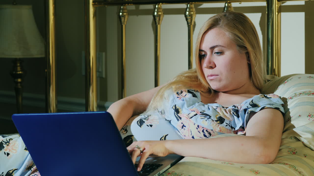 En gravid kvinde slapper af i soveværelset og bruger en bærbar computer.