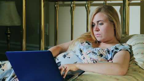 una mujer embarazada se relaja en el dormitorio y usa una computadora portátil