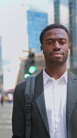 vertical video portrait of young businessman wearing wireless earbuds streaming music or podcast from mobile phone walking to work in offices in the financial district of the city of london uk shot in real time