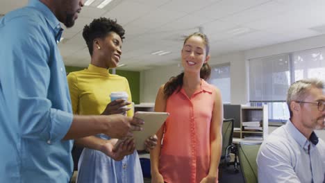 Diverse-male-and-female-business-colleagues-using-tablet-and-talking-in-office