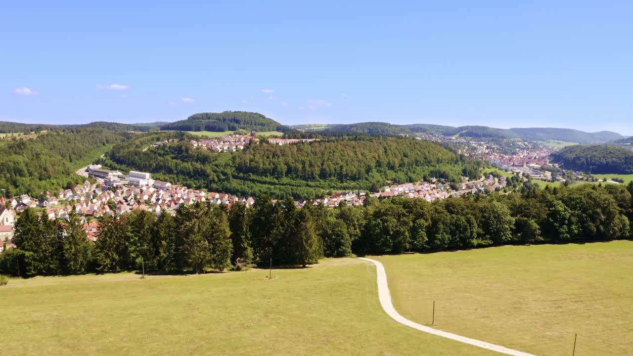 Pull back aerial shot from a yellow field up to the beautiful countryside including a city in a little valley, surrounded by green trees