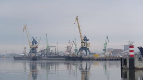 puerto industrial visto desde lejos con grúas altas y agua helada con cielo nublado y cambiante