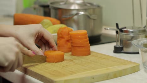 las manos de la ama de casa cortando zanahorias en pedazos en la cocina