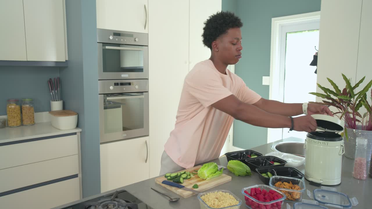 Uomo afroamericano che cucina, taglia su un tagliere, apre il cestino e sistema delle ciotole sull'isola della cucina.