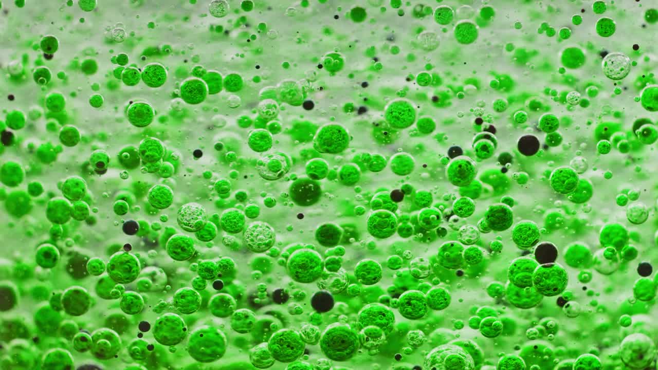 밝은 배경을 가진 물 속에서 천천히 움직이는 녹색과 검은색 거품의 매크로 샷
