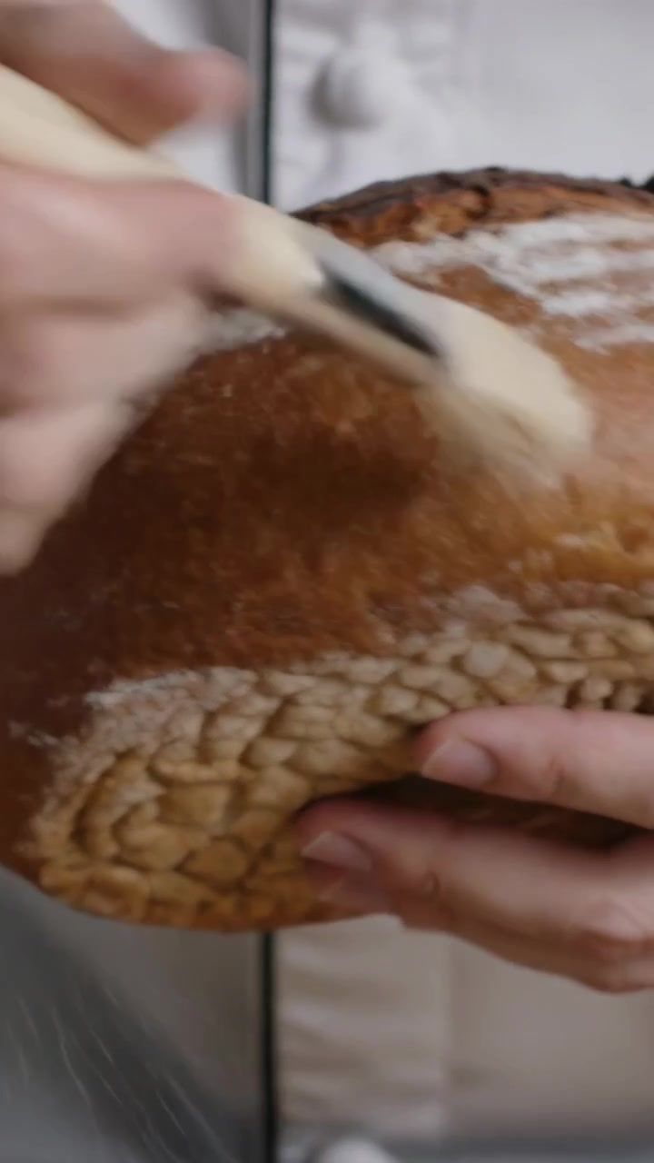 Vertical video: Brush nearing chef in white coat holding loaf at bakery pastry brush clearing flour