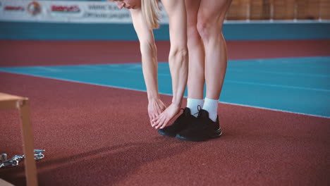 blonde sportswoman warming up and doing standing toe touch exercise in an indoor sport facility