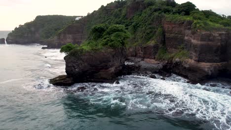 aerial view of waves break on rocks in a blue ocean