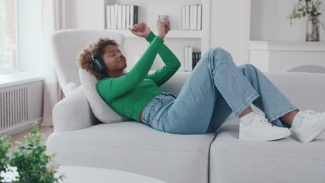 young beautiful ethnic african american woman wearing headphones lying on couch