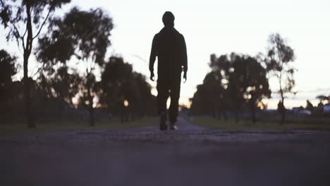 silueta de un hombre caminando por el camino vacío durante la puesta de sol