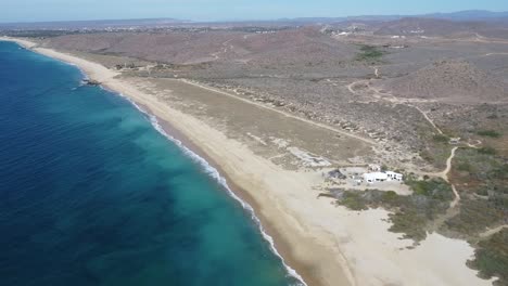 wide drone shot of los cerritos beach on a sunny day with the blue water waves crashing in mexico, todos santos