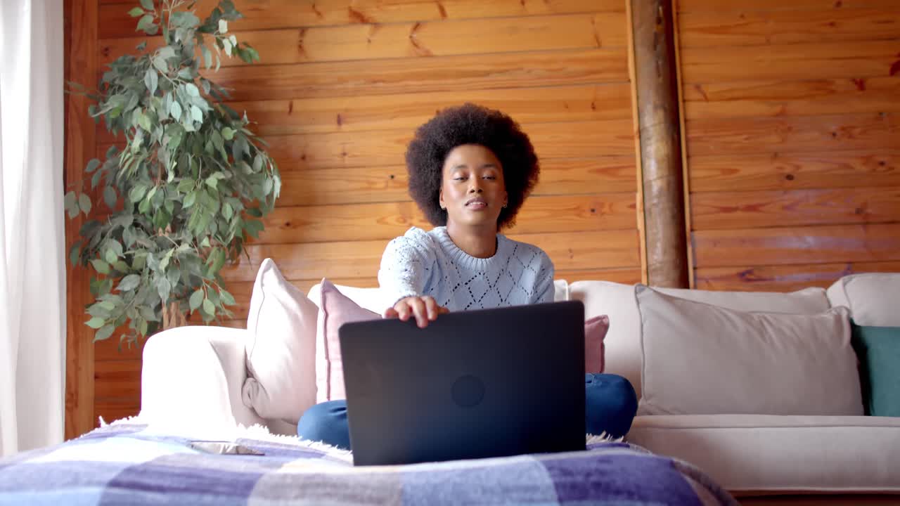 Happy african american woman using laptop in living room, in slow motion