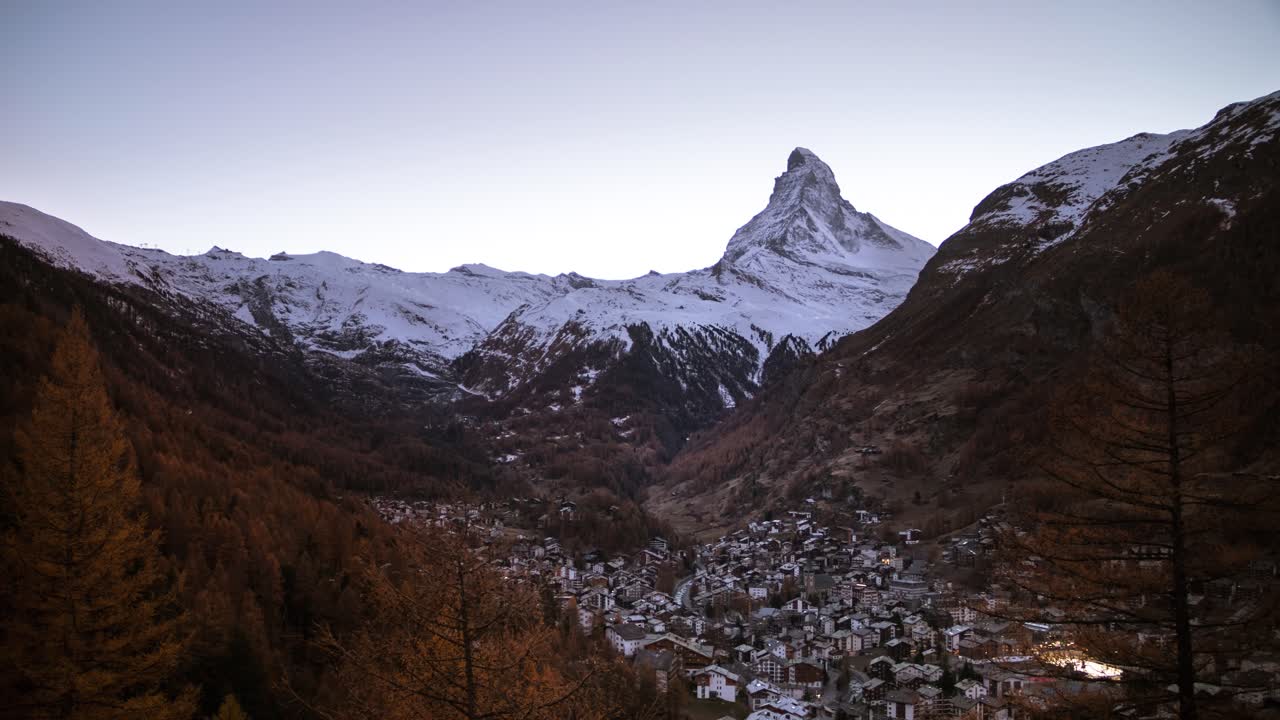 timelapse de día a noche del cervino visto desde zermatt, suiza, mientras las estrellas iluminan el cielo junto con las luces de la ciudad