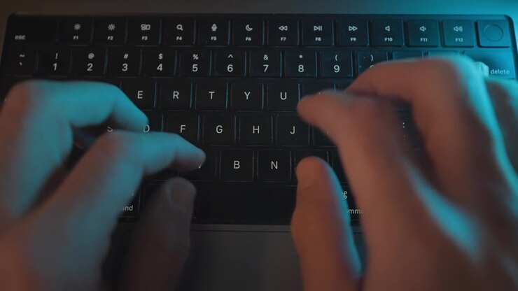 Top view on hands typing on laptop keyboard at night on office or home desk. Man writing programming or coding rapidly pressing on keys and buttons. Hacker working on breaking into secret data server