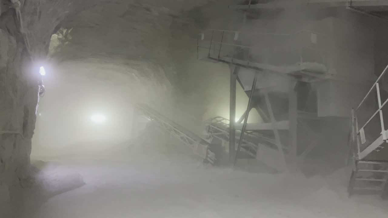 A moving frame capturing salt extraction equipment in a room with high walls and an arch in a salt mine.