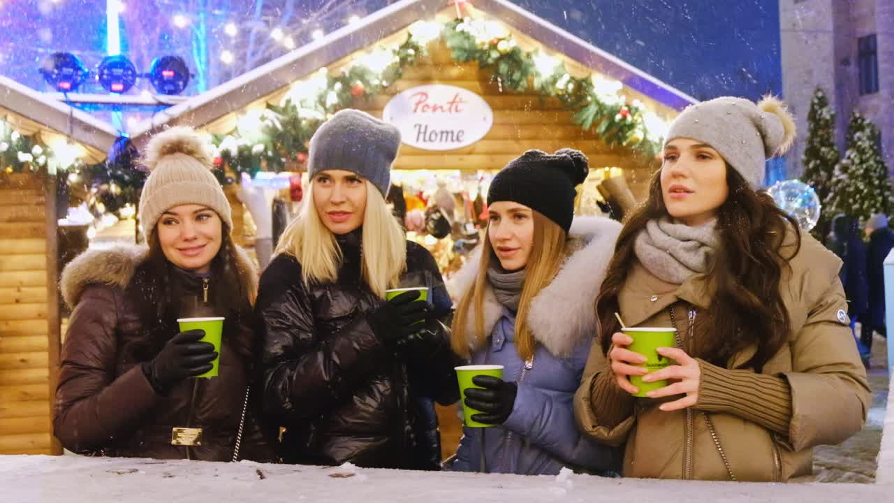 Close-up shot of a group of young female friends celebrating Christmas holiday and drinking coffee at evening in the center of the city