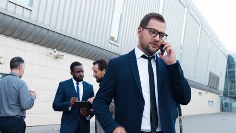 caucasian businessman in stylish clothes and glasses talking on the smartphone in the street