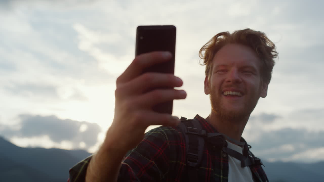 blogger emocionado toma una selfie en el teléfono. hipster alcanza el pico en las montañas.