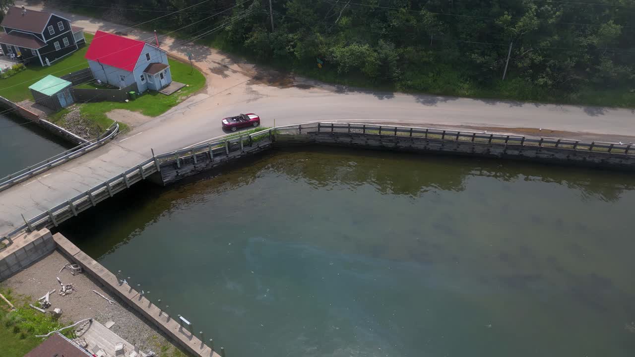 Red convertible sports car driving along ocean coastline and foggy boat harbor