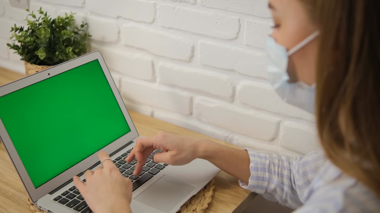 Self-isolation. A girl in a medical mask and striped pajamas at a table. It is trained remotely on a laptop with a green screen. Selective focus..
