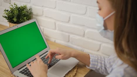 self-isolation. a girl in a medical mask and striped pajamas at a table. it is trained remotely on a laptop with a green screen. selective focus..