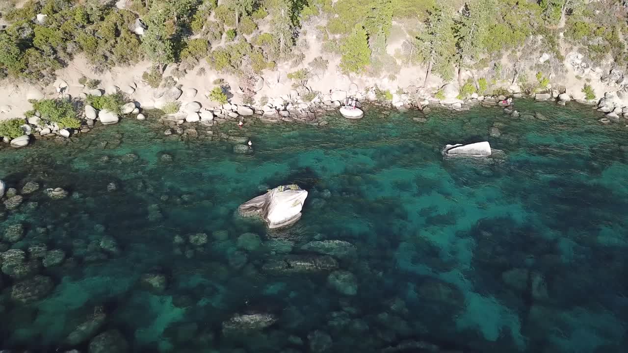 Güneşli bir yaz gününde, ABD Tahoe Gölü'nün berrak alp suyu ve kıyısı ile iğne yapraklı ormanlarının havadan görünümü.
