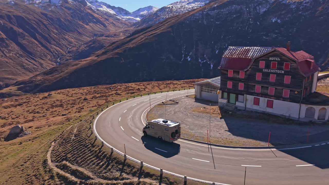 Il traffico scorre lungo la strada del Passo del Furka sotto cieli svizzeri sereni, vista aerea