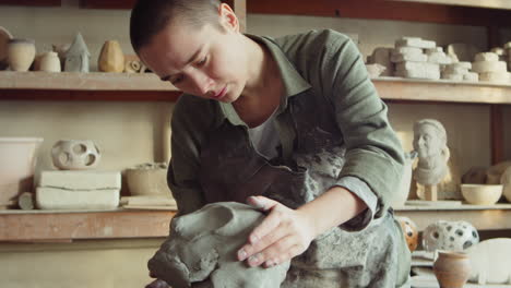 female sculptor creating clay head in workshop