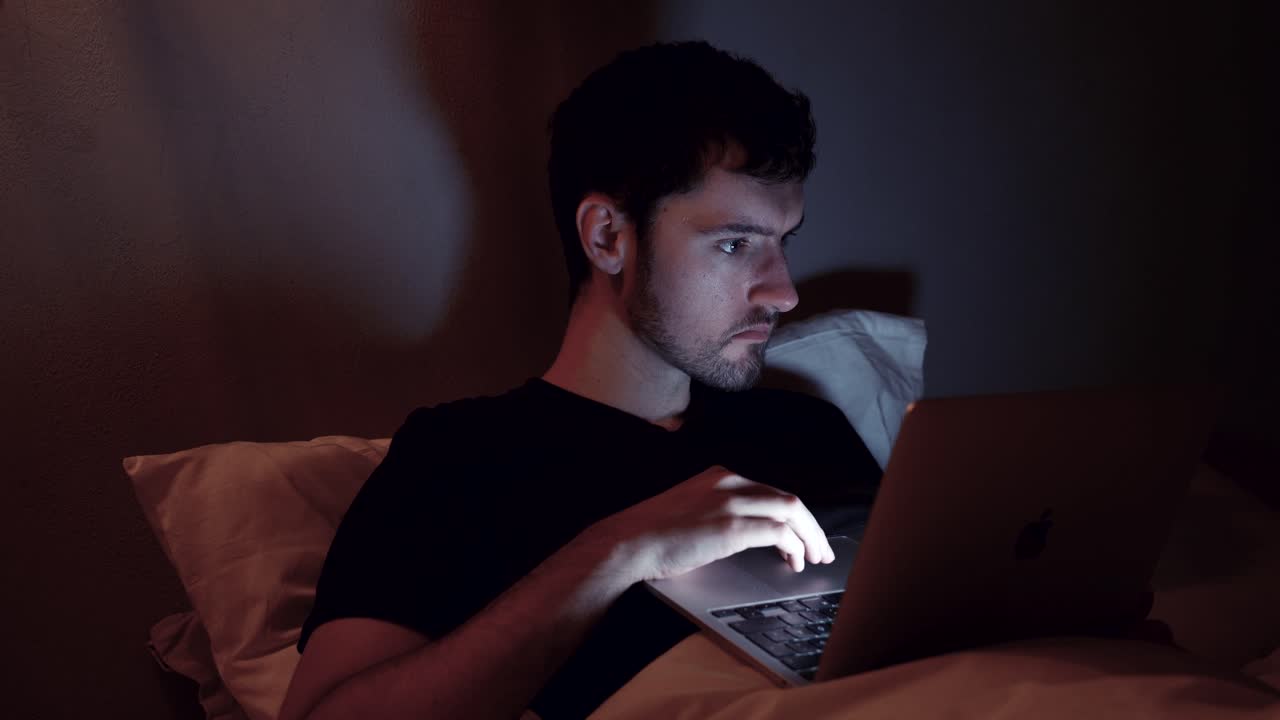 hombre con computadora portátil en la cama, internet en línea por la noche, trabajo tardío, navegación web, video viendo en el cuaderno antes de dormir
