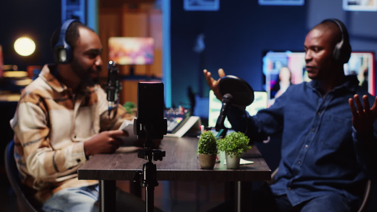 Man on podcast filming with smartphone on tripod while talking with guest during marathon stream