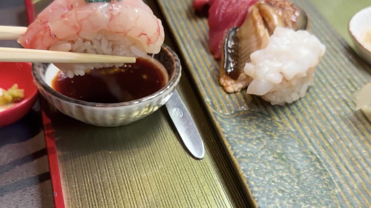 新鮮なエビの寿司を醤油の入ったボウルに浸している人のクローズアップ