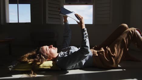 caucasian woman lying on floor holding book and reading in sunny cottage living room