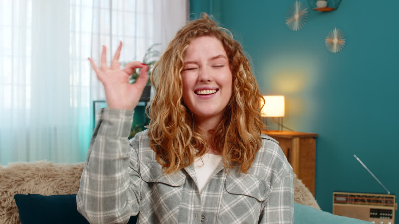 Woman sits on sofa showing ok hand gesture with confident facial expression feeling strong and sure
