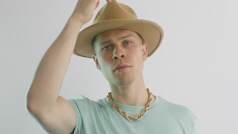 modelo masculino con camiseta verde poniendo un gran sombrero marrón y moviendo la cabeza