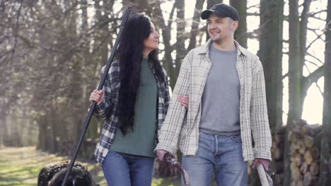 Caucasian couple and their dog holding a wheelbarrow and a rake while they are walking throught the countryside