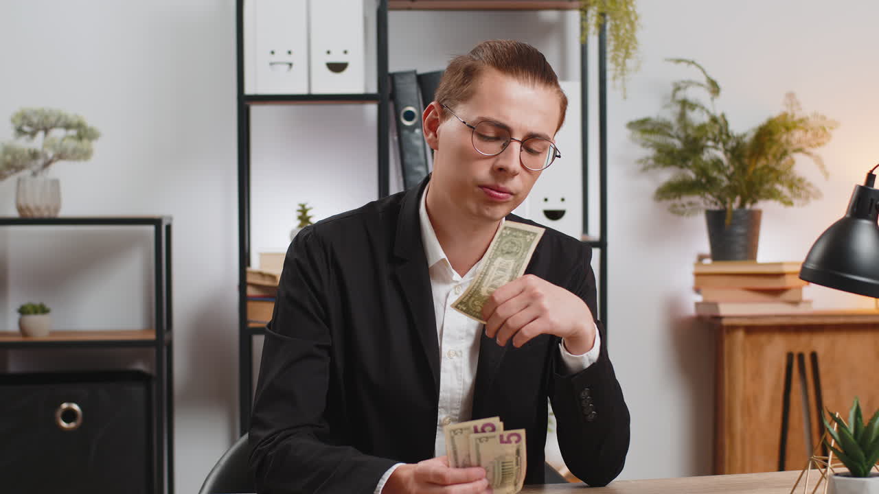 Upset young businessman freelancer counting dollar cash insufficient amount of money at office desk