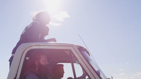 A-couple-stands-in-the-bed-of-a-pickup-truck-as-it-drives-along-a-rural-road