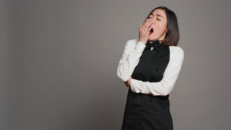 exhausted waitress with apron yawning over grey background