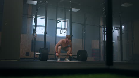 Wide-shot-of-young-Caucasian-extreme-weightlifting-athlete-man-working-out-with-heavy-barbell-in-large-hardcore-gym-hall.