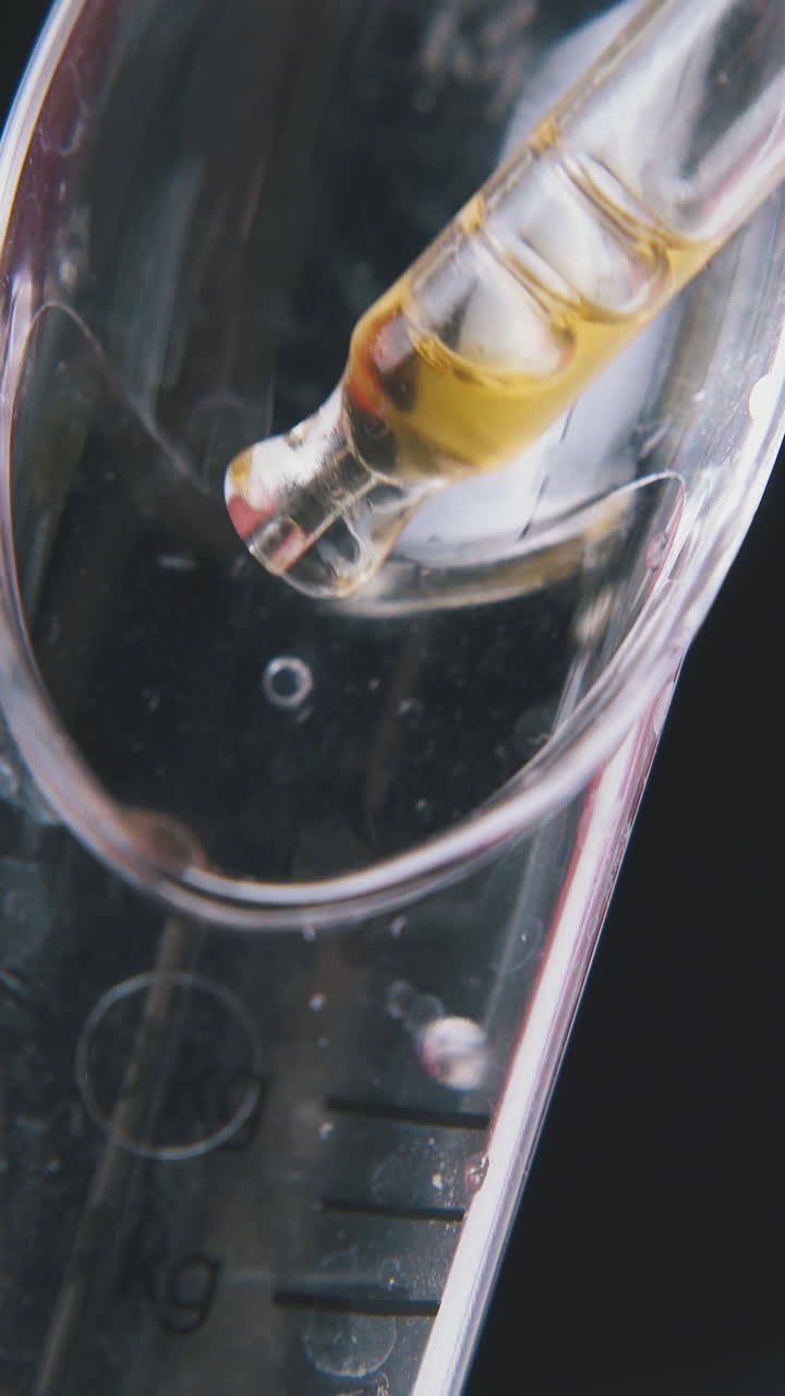 man drops light brown liquid into plastic measuring spoon from pipette on black background extreme close view
